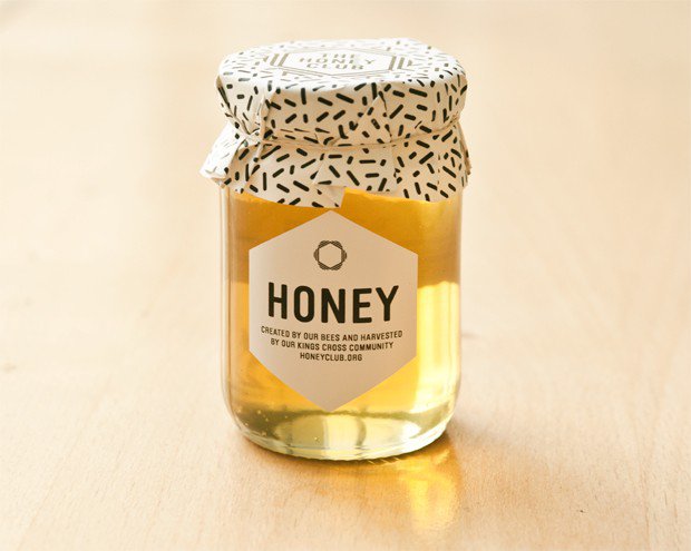 Pote de mel transparente onde um rótulo hexagonal e tampa em papel preto e branco trazem informações do produto.